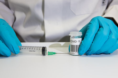 Coronavirus vaccine dose ready for immunisation. Doctor with gloved hands holding a hypodermic...