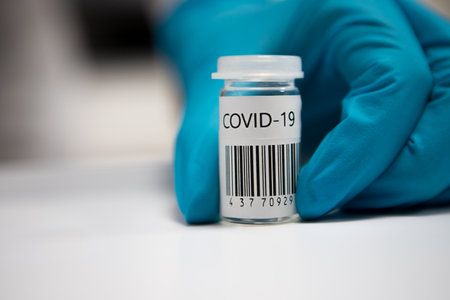 Coronavirus vaccination dose ready for immunisation. Doctor with gloved hands holding a glass vial of covid-19 vaccineの写真素材