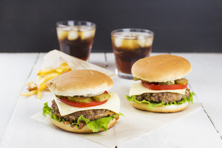 Two mini burgers with meat, lettuce, tomatoes, cheese, pickles, onions, French fries and sparkling water on a white wooden backgroundの写真素材