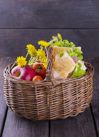 basket for picnic with a sandwich, apple, tomatoes and flowersの写真素材