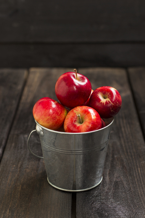 Crop of red apples in metal bucket on a dark wooden backgroundの写真素材