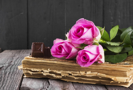 Old book pink roses and chocolate on a dark wooden backgroundの写真素材