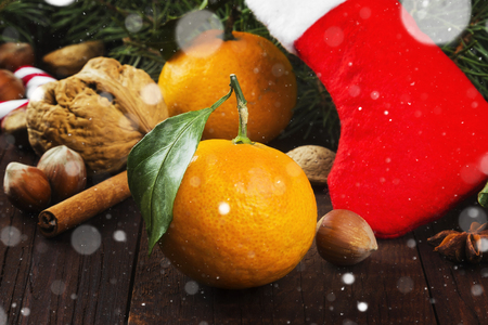 Gift in Christmas sock - tangerine, candy, nuts, cinnamon on a dark wooden background. Toning.の写真素材