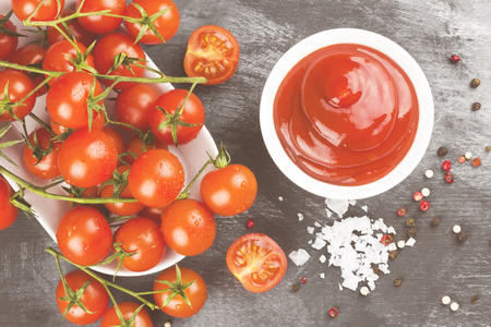 Tomato sauce in white bowl, spice and cherry tomatoes on a dark background. Top view. Food background. Toning.の写真素材