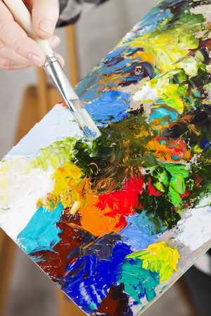 The girl artist holds a brush and a wooden palette with various art oil paints.の写真素材