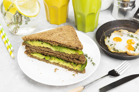Breakfast - a toast from rye bread with avocado, fried eggs, lemonade and coffee on a light backgroundの写真素材