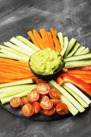 Traditional Latin American sauce guacamole in a bowl and various vegetables (carrots, tomatoes, cucumbers, celery) on a dark backgroundの写真素材