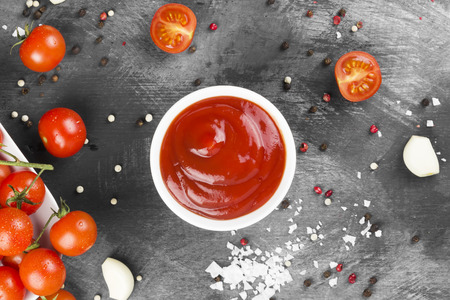 Tomato sauce in white bowl, spice and cherry tomatoes on a dark background. Top view.の写真素材