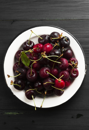 Fresh sweet cherry in a white plate on a dark wooden background. Top view. Food background.の写真素材