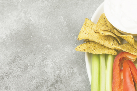 Creamy sauce in white bowl, various vegetables (celery, pepper) and nachos. Top view, copy space....