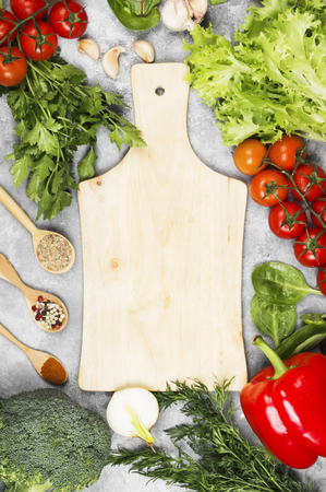 Assortment of fresh vegetables (pepper, cherry tomatoes, onions, garlic, spinach, broccoli) and spices on a light background. Wooden cutting board. Top view, copy space. Food backgroundの写真素材