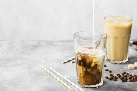 Milk pouring in ice coffee in a tall glass on a gray background. Copy space. Food background. Toningの写真素材