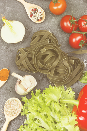 Raw pasta of tagliatelle with spinach and ingredients for cooking (cherry tomatoes, spices, garlic, spinach leaves, pepper, lettuce) on a dark background. Top view. Food background. Toningの写真素材