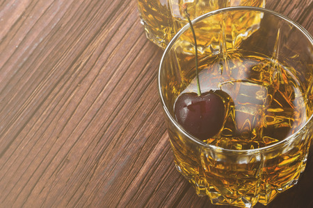 Cocktail from whisky with cherry in two glasses on a wooden background. Copy space. Food background....