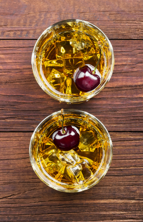 Cocktail from whisky with cherry in two glasses on a wooden background. Top view. Food backgroundの写真素材