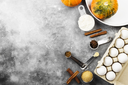 Ingredients for pumpkin pie - flour, pumpkins, eggs, cane sugar, various spices (nutmeg, ginger, cinnamon, anise) and white round baking dish on a gray background. Top view, copy space. Food backgroundの写真素材