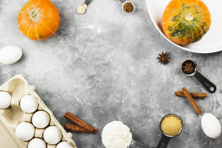 Ingredients for pumpkin pie - flour, pumpkins, eggs, cane sugar, various spices (nutmeg, ginger, cinnamon, anise) and white round baking dish on a gray background. Top view, copy space. Food backgroundの写真素材