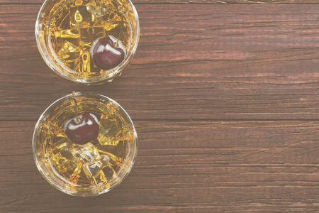 Cocktail from whisky with cherry in two glasses on a wooden background. Top view, copy space. Food background. Tonedの写真素材