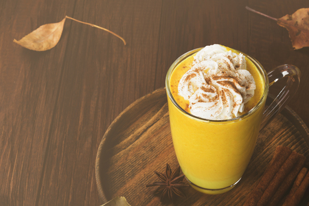 Pumpkin latte with spices (cinnamon, anise) and whipped cream on a wooden background. Copy space. Food background. Tonedの写真素材