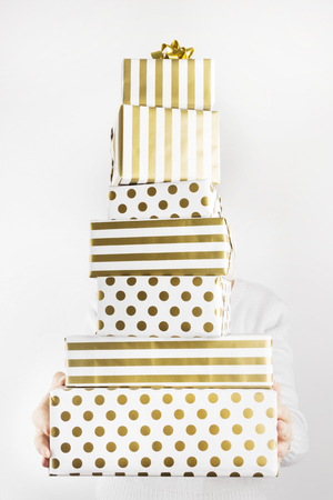 Woman holding group of gifts in white and gold paper on a gray backgroundの写真素材
