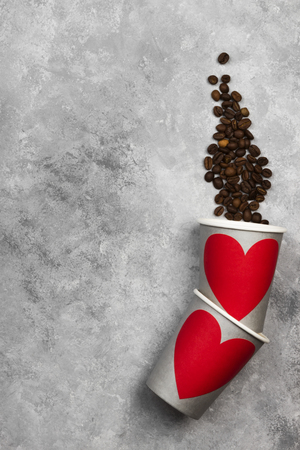 Concept love to coffee. Gray paper cups for drinks with red heart, coffee beans on a light background. Top view, copy space. Food background.の写真素材