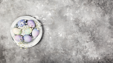 Multicolored eggs for Easter in marble plate with white flowers on gray background. Top view, copy space. Food backgroundの写真素材