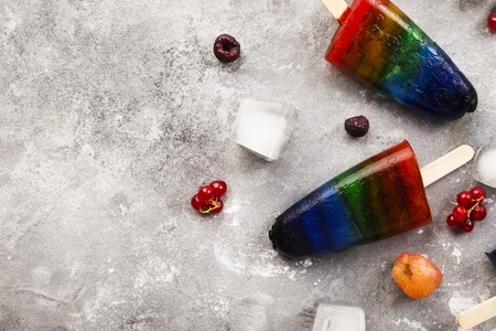 Rainbow colorful ice cream with raspberry yellow and red, blackberry, currant with wood stick on...