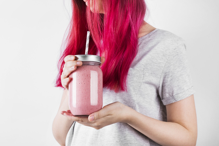 Young woman with pink hair drinks smoothies from berries and fruits. Concept meals to goの写真素材
