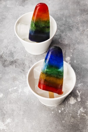 Rainbow colorful ice cream with wood stick in white bowls on gray backgroundの写真素材