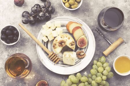 Snacks with wine - various types of cheeses, figs, nuts, honey, grapes on a gray background. Top view. Food background. Tonedの写真素材