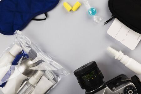 Set for flight small bottles with cosmetics, sleep mask, camera, earplugs, nasal spray, air ticket and documents on gray background. Top view, copy spaceの写真素材