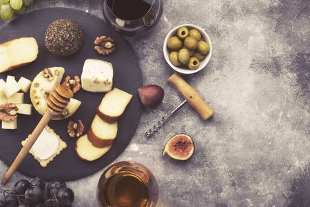 Snacks with wine - various types of cheeses, figs, nuts, honey, grapes on a gray background. Top view, copy space. Food background. Tonedの写真素材
