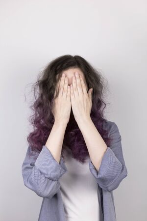 Young girl hides in palms face. Coloring purple hair.の写真素材