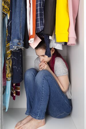 Young girl sits in wardrobe clogged into corner. House violenceの写真素材