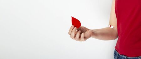 Young girl in red T-shirt holds drop in her hand, the second hand taped with patch with red heart after giving blood on grayの写真素材