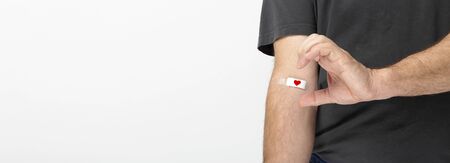 Man in gray T-shirt hand taped with patch with red heart after giving blood on gray