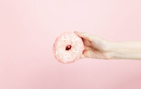Woman hand holds donut with pink icing and coconut pastry topping on pink