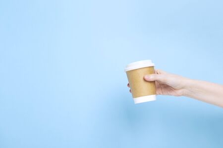 Woman holds hand paper cup with coffee on blueの写真素材