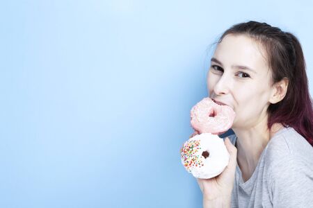 Young girl holds two donuts in her hand and bites one