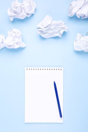White notebook and pen on blue background around crumpled paper in the form of clouds. Concept of drawing up wish list and dreams, head in the cloudsの写真素材