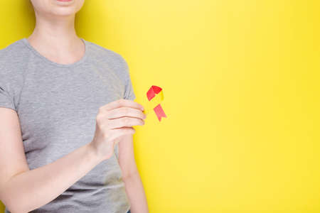 World hepatitis day concept. Girl in gray T-shirt holds in her hand awareness symbol red-yellow ribbon. Yellow background. Copy spaceの写真素材