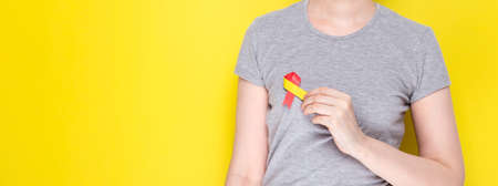 World hepatitis day concept. Girl in gray T-shirt holds in her hand awareness symbol red-yellow...