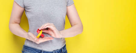 World Hepatitis Day Concept. Girl in gray T-shirt holding red-yellow ribbon area liveras symbol of awareness. Yelow background. Copy spaceの写真素材