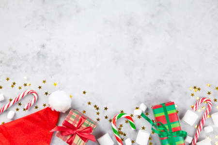 Christmas composition. Gifts, caramel cane, marshmellow, santa hat on gray concrete background with sparkling stars. Concept of winter holidays, new year, Christmas. Top view. Copy spaceの写真素材