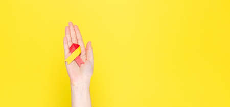 World Hepatitis Day concept. Woman holds in her hand awareness symbol red-yellow ribbon. Copy space