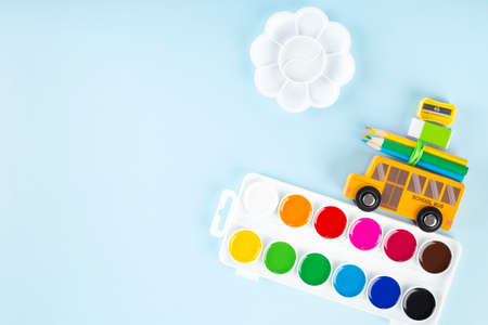 Back to school concept. Drawing accessories. Toy school bus drives watercolor, on blue background....