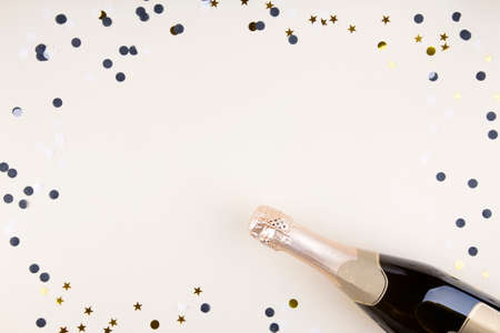 Holiday attributes. Bottle of champagne, confetti for new year on beige background. Top view. Copy space