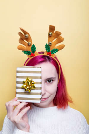 Girl in white sweater and deer horns on head, holds gift in hand, yellow backgroundの写真素材