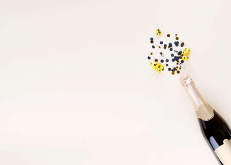 Holiday attributes. Bottle of champagne and confetti in form of splashes for new year on beige background. Top view. Copy spaceの写真素材