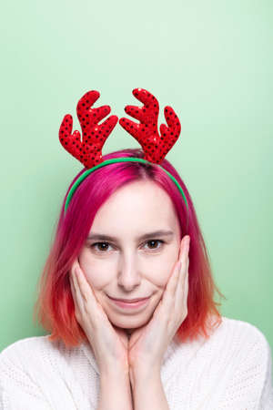 Happy woman in white sweater and deer horns brings her hands to face and smiles, green backgroundの写真素材